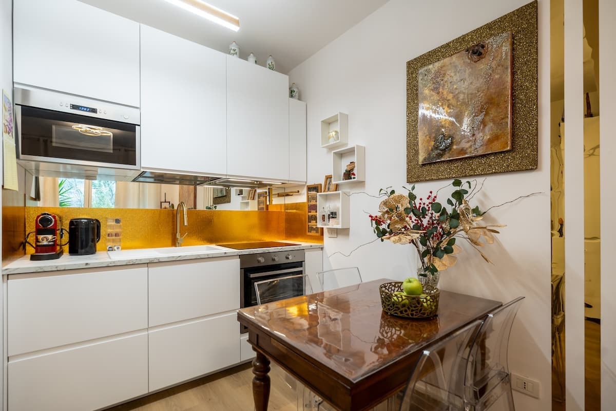 Cucina bianca con paraschizzi dorato e tavolo in legno